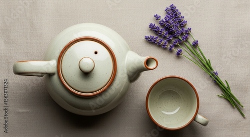 A light beige tea set, teapot and cup, with a small bunch of lavender, arranged on a neutral surface. photo
