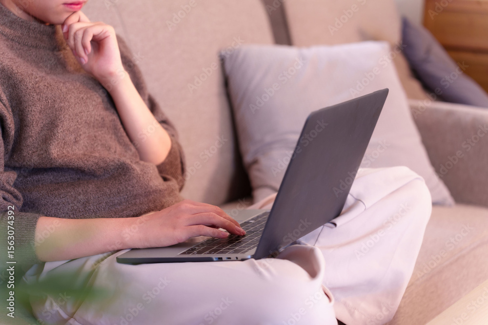 Naklejka premium Asian young adult woman immersed in artificial intelligence daily work from home on laptop on sofa comfortable remote productivity