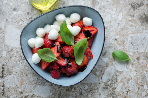 Bowl of strawberry caprese with mini mozzarella and basil on a brown granite background, horizontal shot, high angle view
