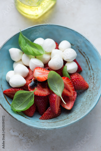 Caprese with fresh strawberry, mini mozzarella cheese and fresh basil in a turquoise bowl, vertical shot, middle close-up