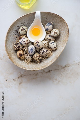Bowl with raw fresh quail eggs on a light-beige marble background, vertical shot, copyspace, top view