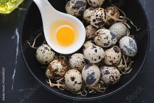 Close-up of fresh uncooked quail eggs in a black bowl, horizontal shot, elevated view