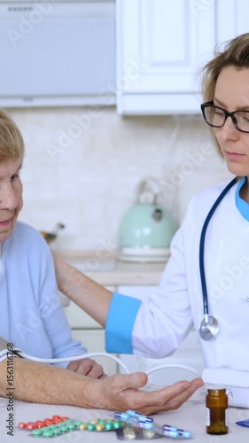 Vertical screen home doctor measuring blood pressure of a senior woman while holding her hand with care and empathy, with pills on the table