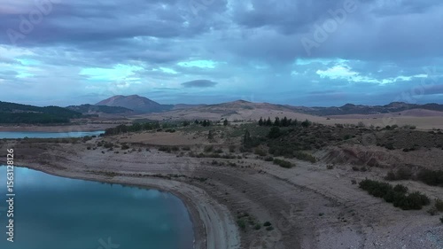 Aerial view flying along dry shoreline of reservoir, showing low water levels. Powerful visual of drought, heatwave and climate change impact, Andalusia, Spain