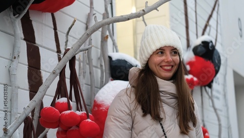 Portrait of a beautiful young woman in winter clothes. The woman smiles happily against the backdrop of a winter street traditionally decorated for Christmas holidays. The woman poses for the camera
