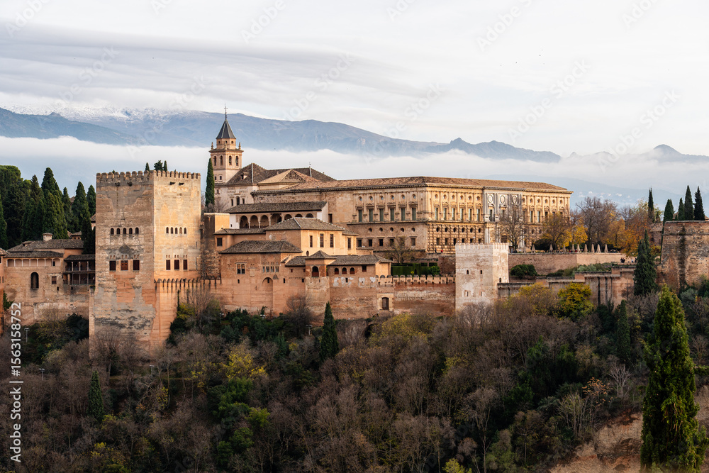 Obraz premium The Alhambra in Granada, Spain, with the Sierra Nevada mountains in the background at sunset. This historic site is a key tourist destination in Andalusia.