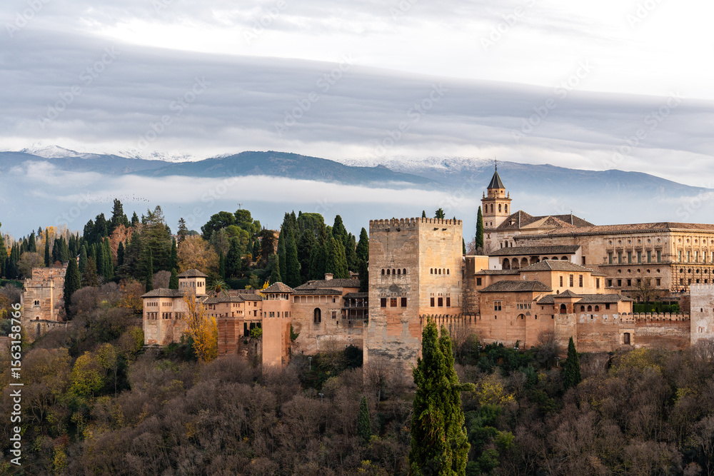 Obraz premium The Alhambra in Granada, Spain, with the Sierra Nevada mountains in the background at sunset. This historic site is a key tourist destination in Andalusia.