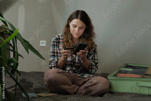Online payment, booking a last minute tour. Woman paying for trip using bank card and smartphone