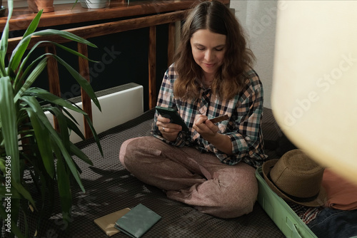 Online payment. Woman books a last minute tour using bank card and smartphone at home 