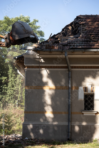 Heavy duty excavator demolishing an old house. Detail on the shingle roof demolish.