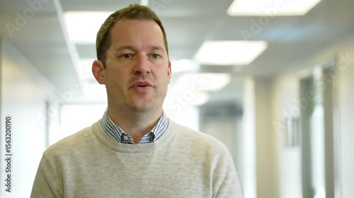 Confident businessman in office hallway talking to camera