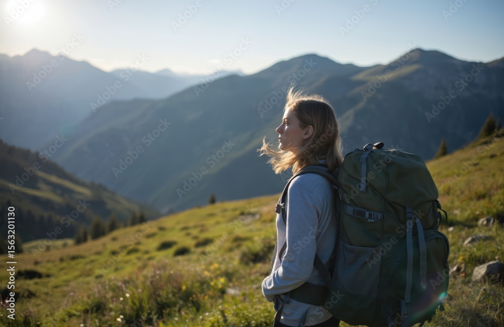 Naklejka premium Young woman with backpack hiking in mountains. Girl enjoys nature, landscape. Person looks at mountain range. Healthy lifestyle, travel, vacation, adventure. Hiker explores outdoor recreation.