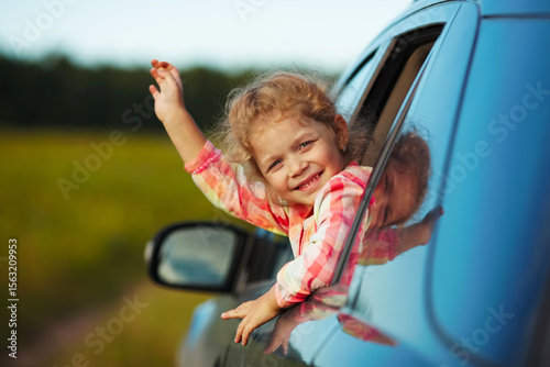 Litle cheerful girl waving from the car.