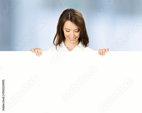 Image - happy smile brunette business woman businesswoman stand behind, peeping, point white blank banner mockup signboard. Success advertise concept. Free ad text space. Blurred office background
