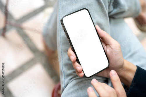 Fotografie Hand holding white screen smartphone over lap using application or social media while sits on bench