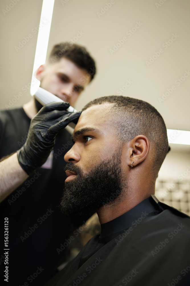 Fototapeta premium Blurred barber trimming head of bearded african american customer