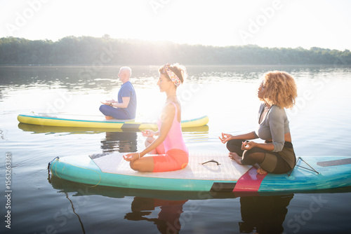 Diverse Group Practicing SUP Yoga on a Scenic Lake at Sunset.
