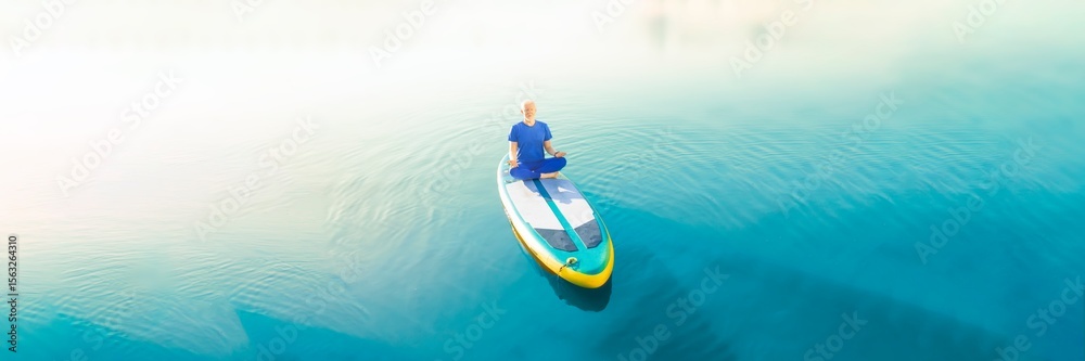 Obraz premium A man doing yoga on his SUP board and practicing mindfulness on his travel.