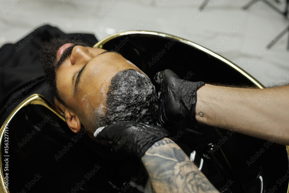 Obraz premium Barber washing hair of african american man in barbershop 