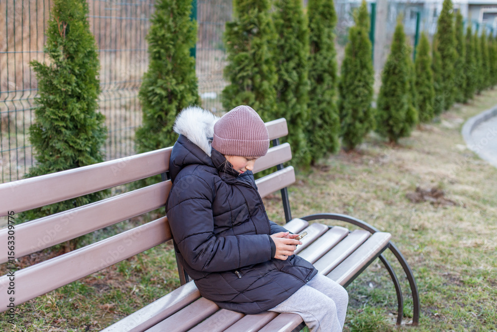 Fototapeta premium Kid using phone alone on park bench