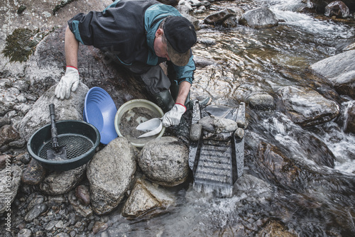 Outdoor adventures on river. Gold panning in a mountain creek, search for gold in winter. Man is looking for gold with a sluice box, sieve, gold pan and shovel
