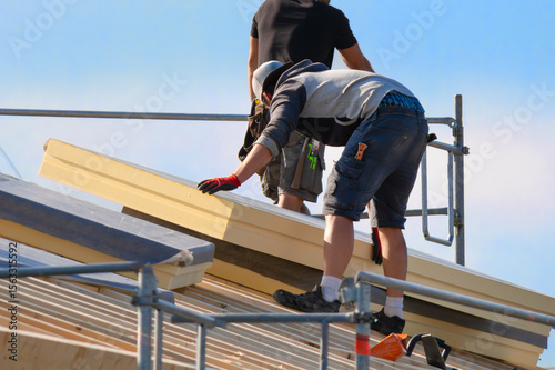 Construction worker installing large insulation panels on a roof. Energy-efficient renovation, sustainable building practices, and climate protection in the housing sector.