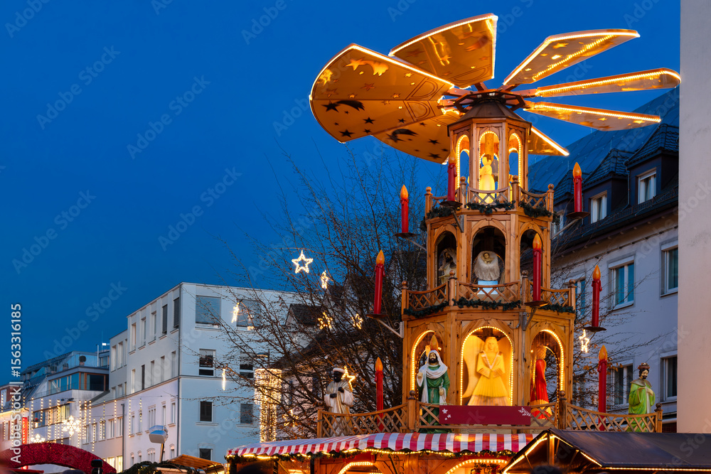 Naklejka premium Traditional Christmas market with lights, wooden stalls and Christmas pyramid in downtown Bregenz, Lake Constance, Austria