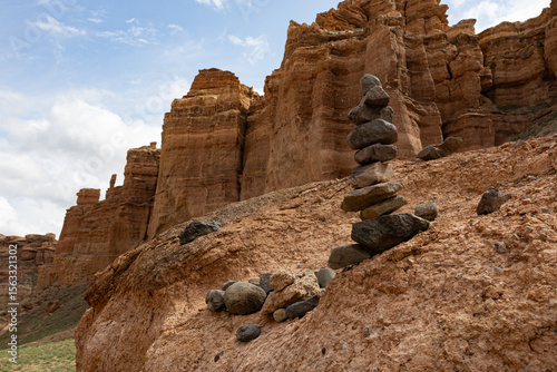 A tower of balanced stones stands on a rocky hill in Charyn Canyon, surrounded by impressive sandstone cliffs under a blue sky