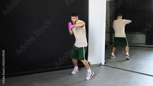 Man practices boxing techniques in a gym with a mirror reflection