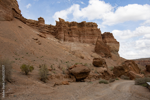 Large boulders and rugged cliffs rise above a dirt path in the dramatic landscape of Charyn Canyon, Kazakhstan
