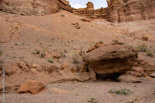 A large boulder rests on a dry, rocky slope with sparse desert vegetation in Charyn Canyon, Kazakhstan