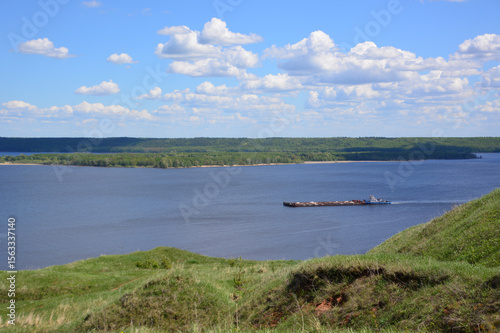 Serene river landscape with a barge under a cloudy blue sky