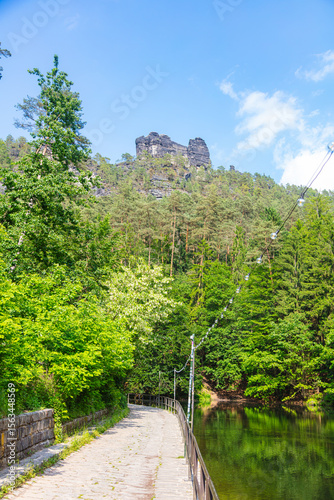 Scenic forest trail leading to the famous Bastei Bridge in Saxon Switzerland, Germany. Surrounded by lush greenery, sandstone cliffs and a small dam, this popular route offers pure hiking charm