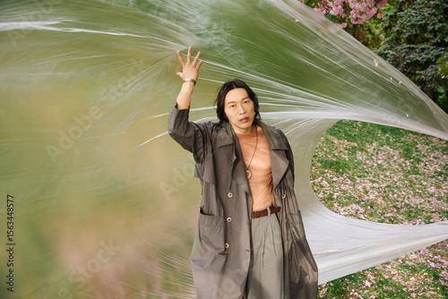 Fotografie Stylish young man in grey outfit poses creatively in a vibrant park setting
