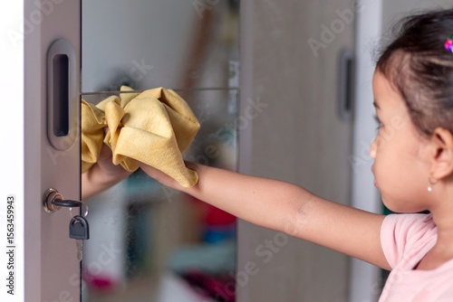 A little Asian girl cleaning and wiping mirror with a chamois cloth