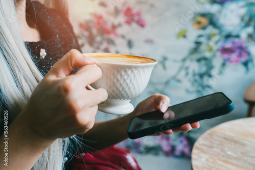 Woman Holding Coffee Cup While Using Smartphone in Cozy Cafe with Floral Background
