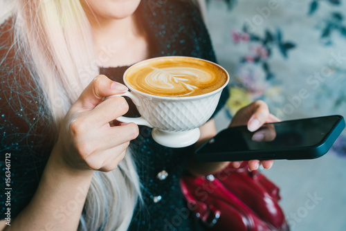 Coffee in cafe. Young Woman Enjoying Latte Art with Smartphone in Stylish Cafe Setting