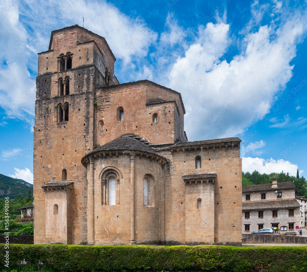 Fototapeta premium Romanesque church of Santa Cruz de los Seros Spain standing under vivid sky massive stone walls apse and bell tower dominate village scene symbolizing medieval faith history architectural strength