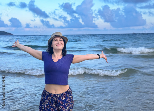 A joyful woman standing by the ocean with open arms, embracing nature and freedom, happy woman enjoying freedom at the sea with arms wide open, horizontal shot