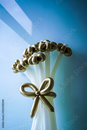 Elegant golden and white balloon bouquet with a decorative bow against a soft blue background, perfect for celebrations, anniversaries, or special events.