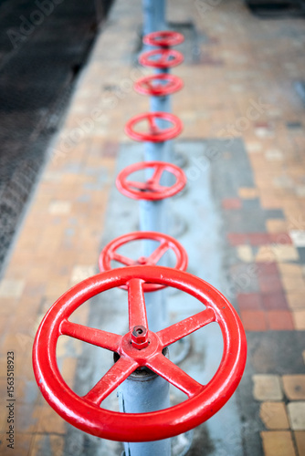 Row of old retro valve wheels painted red selective focus with extension device over out of focus background tiled floor and perforated metal sheet stamping plates, with copyspace.