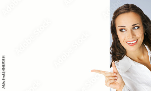 Image - happy smile brunette business woman businesswoman stand behind, peeping, point finger white blank banner mockup signboard. Advertise concept. Free ad text space. Isolate grey gray background