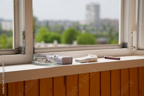 An open window and an ashtray with cigarettes on the windowsill, a smoking area in the house, the harm of tobacco use.