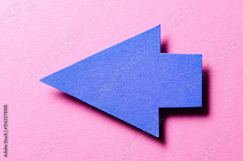 Blue cut out blank paper cardboard arrow direction sign with copy space for text on pink background, flat lay top view pointing symbol conceptual message backdrop photo