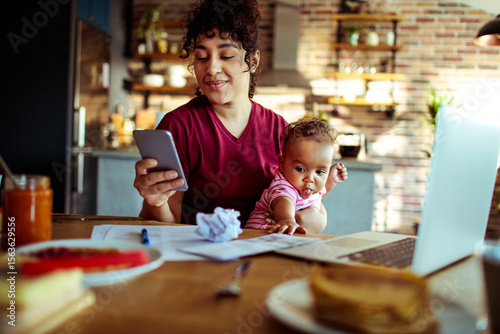 Work from home mom with baby on video call in kitchen
