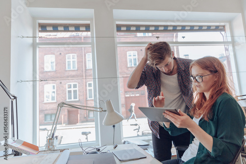 Young coworkers discussing project while looking at tablet in modern office