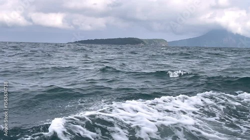 Anak Krakatau view in Lampung Indonesia. Dark glowing clouds above the open sea and evergreen forest. Dramatic sky, epic seascape. A view from the yacht. Nature, environment, climate change