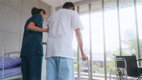 Beautiful asian woman physiotherapist assists Asian man patient in walking exercises using crutches in physical therapy clinic.