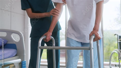Beautiful asian woman physiotherapist assists Asian man patient in walking exercises using crutches in physical therapy clinic.