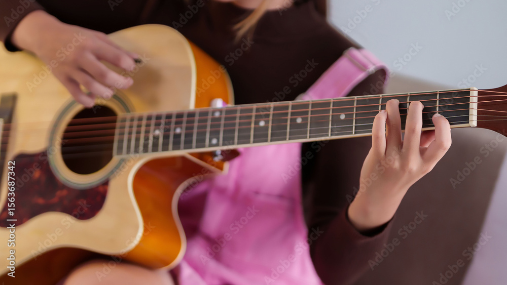 Fototapeta premium Young Asian woman playing acoustic guitar at home for relaxing and enjoy music hobby